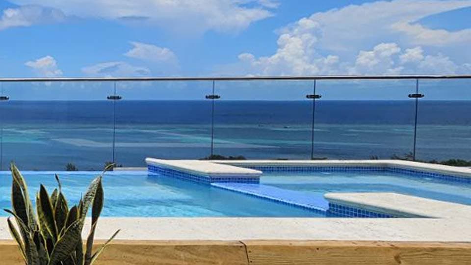 Moderno apartamento frente al mar con sala de estar de planta abierta con cocina blanca totalmente equipada, elegante juego de comedor y cómodo sofá gris. Los grandes ventanales ofrecen impresionantes vistas al océano, mientras que la decoración de temática costera y un balcón privado realzan el ambiente junto al mar. Ideal para alquileres vacacionales de lujo o para una vida costera contemporánea.